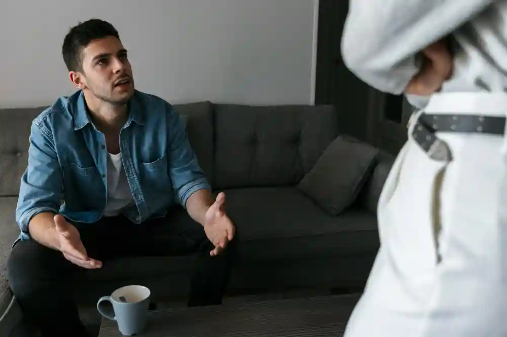 Man sitting on a couch explaining emotional concerns during a therapy session.