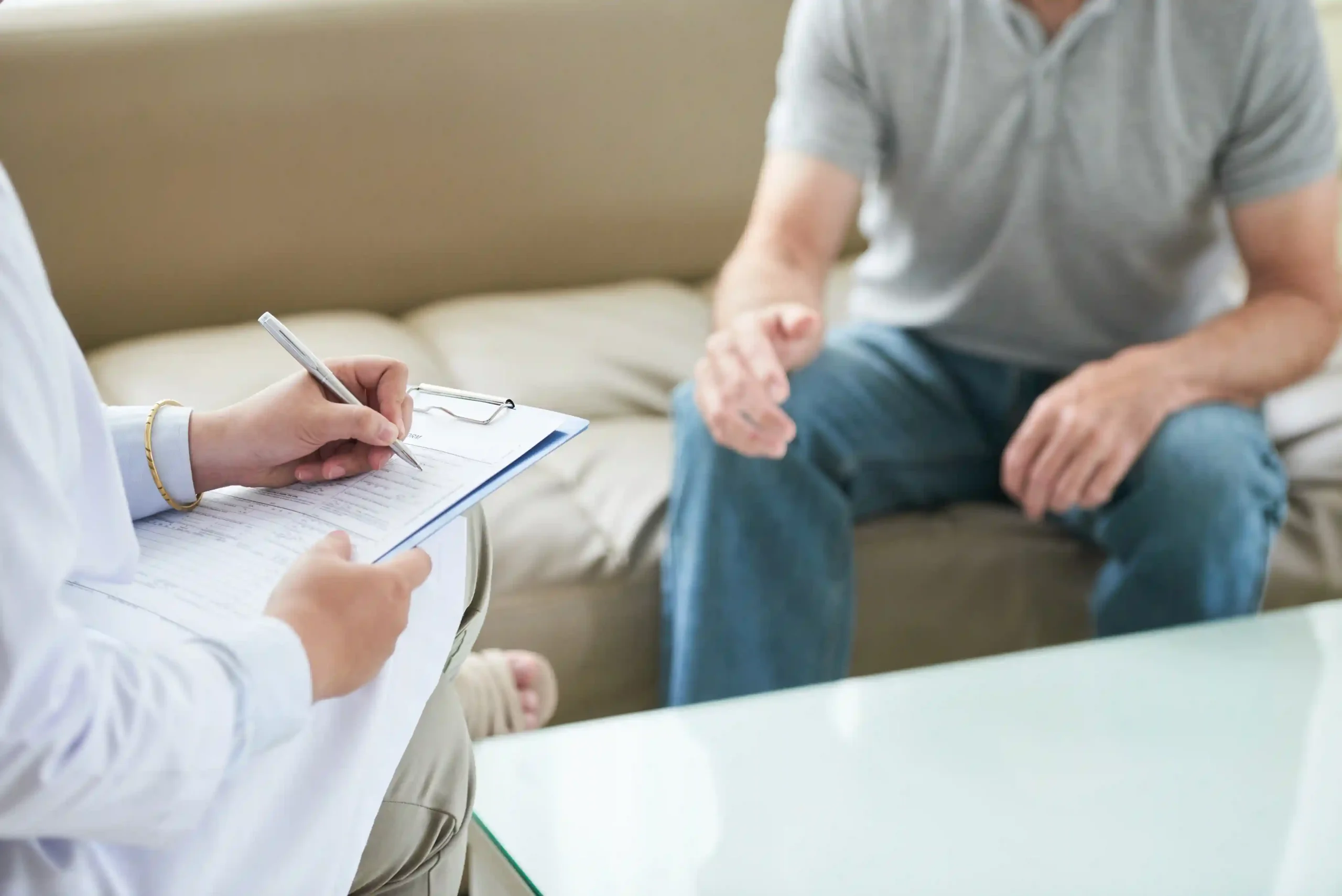 A therapist takes notes during an in-person individual therapy session with a male patient