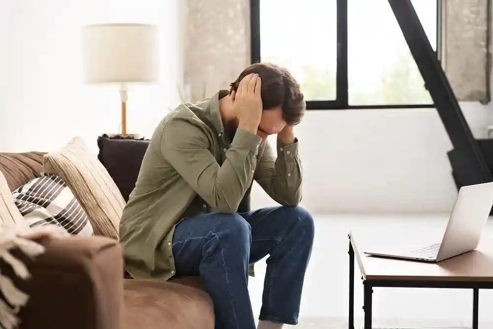 Man sitting on a sofa holding his head, showing signs of severe stress