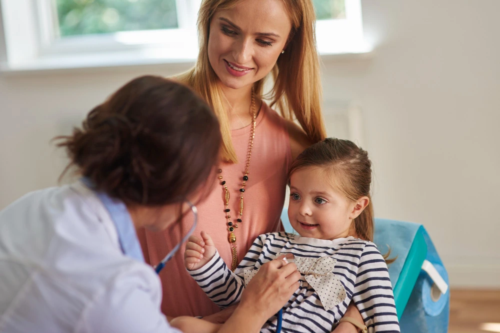 Primary care doctor examining a young child with a stethoscope while the mother looks on during a wellness visit at Mothermind Tampa