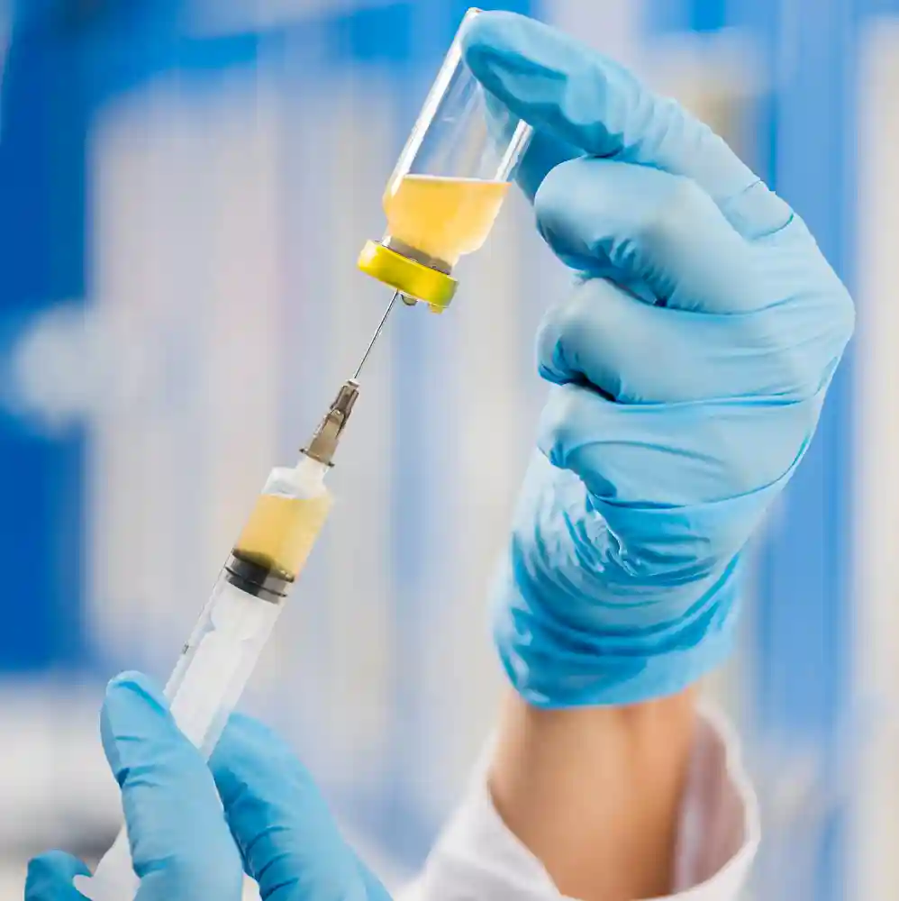 Close-up of gloved hands drawing IV vitamin solution from vial into syringe