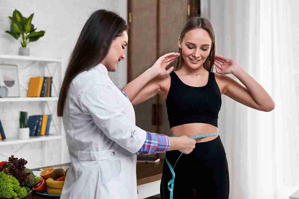Doctor measuring patient's waist with tape measure during weight loss consultation